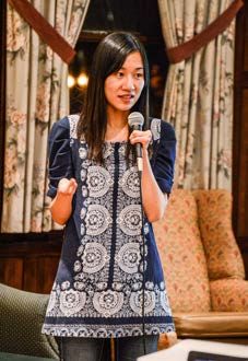 A photo of Sandie Yi standing and holding a microphone.