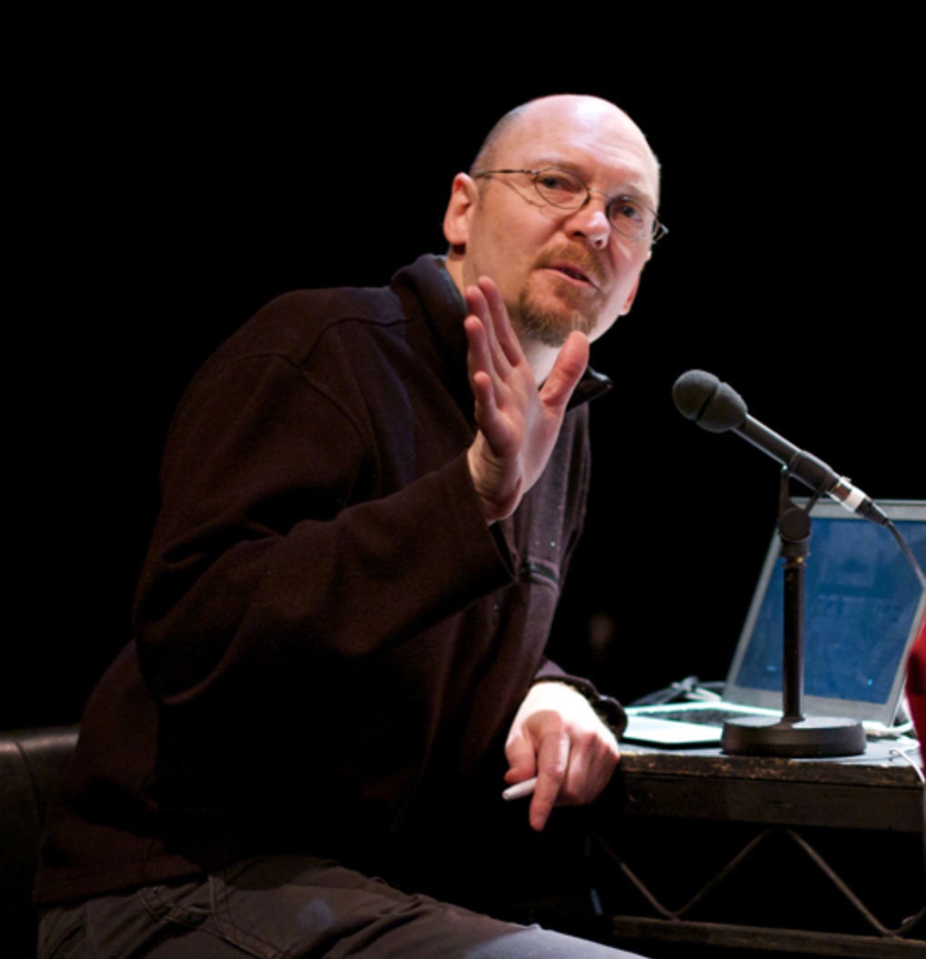 A photo of Robert Sember sitting at a desk with a laptop and a microphone.