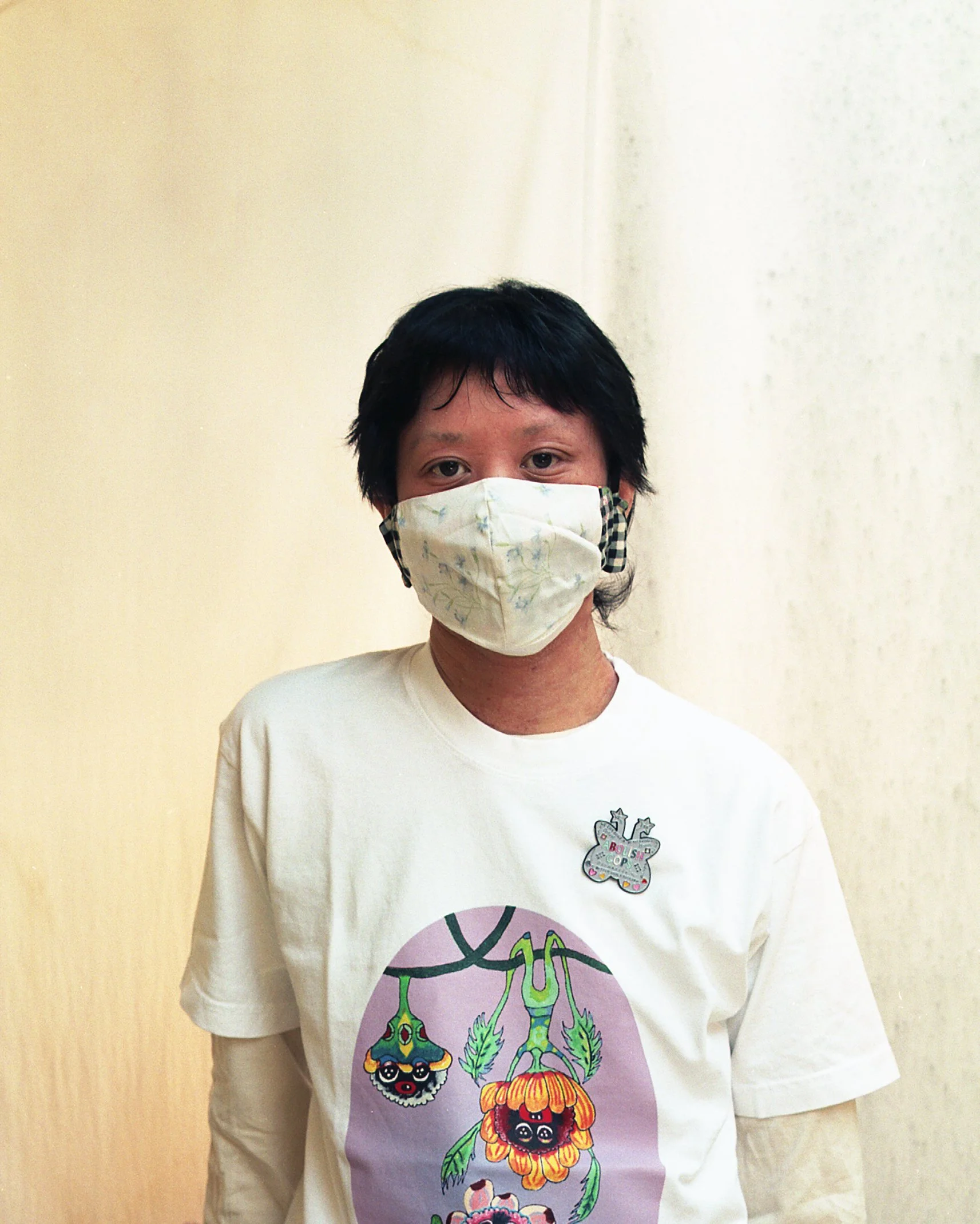 A photo of Thai Lu wearing a white t-shirt with brightly colored characters on it, and a cloth mask.